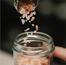 Pink bath salts being poured into a glass jar